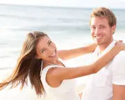 Happy couple on beach in love having fun holding around each other hugging looking at camera. Lifestyle portrait of healthy young interracial multi-ethnic newlywed couple on honeymoon. Asian woman.