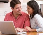 Couple in kitchen using laptop and smiling